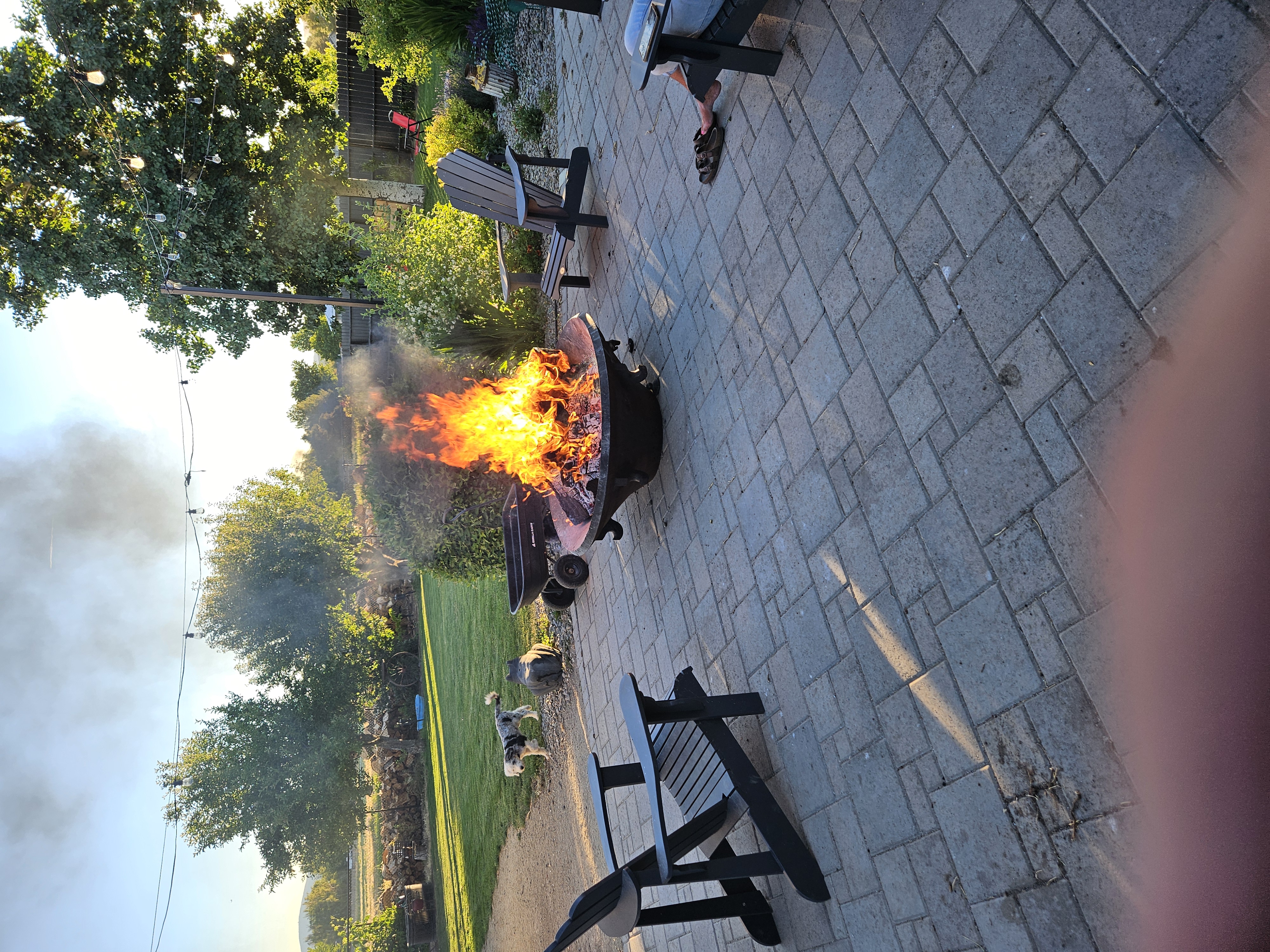 Sunset photo of a custom paver patio with a glowing fire bowl, Adirondack chairs, and landscaped garden