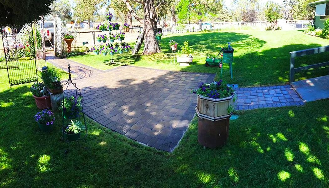 Daytime view of a paver pathway through a green yard with vertical hanging flower planters and garden features